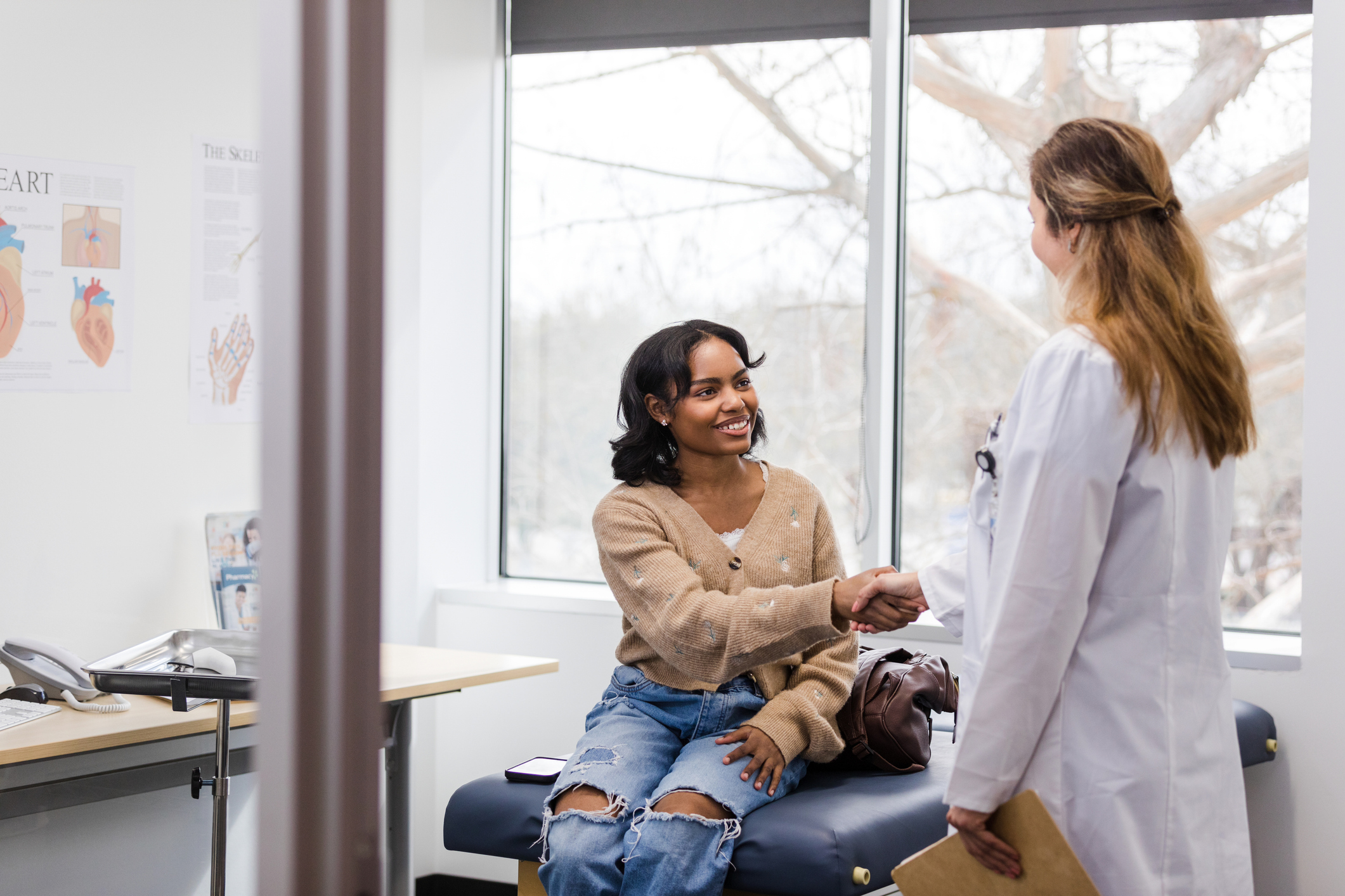 Patient smiling on exam table shaking doctor’s hand