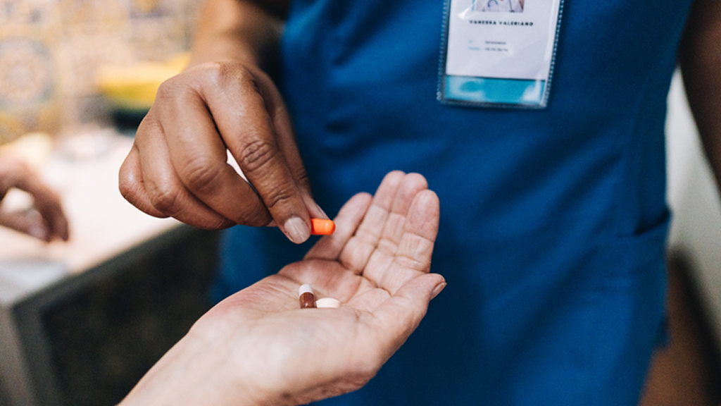 Healthcare worker placing pill into patient's hand