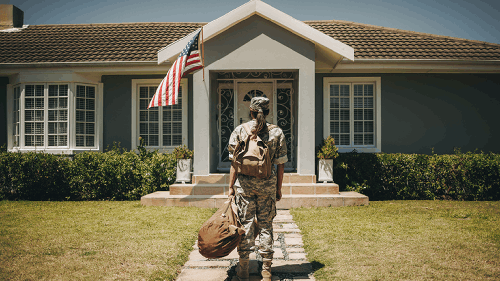 Soldier carrying duffel bag standing before house