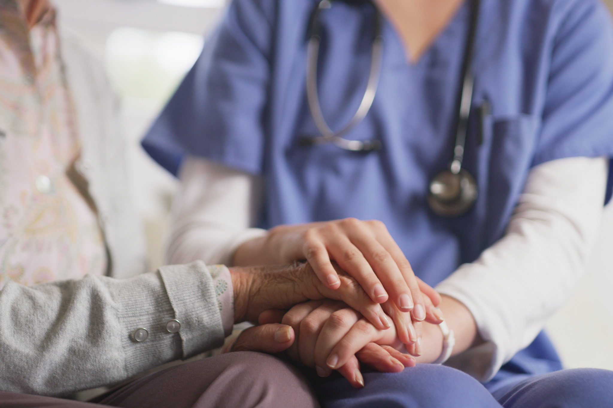 Nurse holding elderly patient's hands in comfort